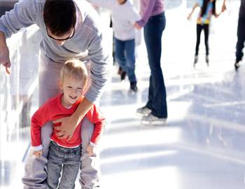 Man holding onto son at an ice skating rink