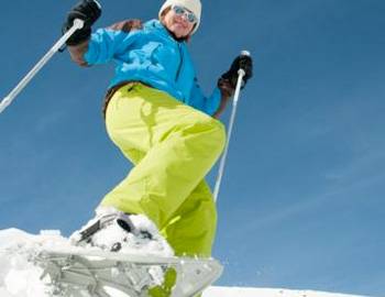 A woman snowshoeing with poles on a bluebird day